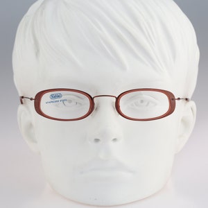 May include: Brown oval-shaped eyeglasses with a thin metal frame and the text "Sahlo Stainless Steel" on the left lens. The glasses are displayed on a white mannequin head.