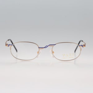 May include: A pair of gold-rimmed glasses with blue accents. The glasses have a rectangular shape and say "TASSI Made in Japan" on the right lens.