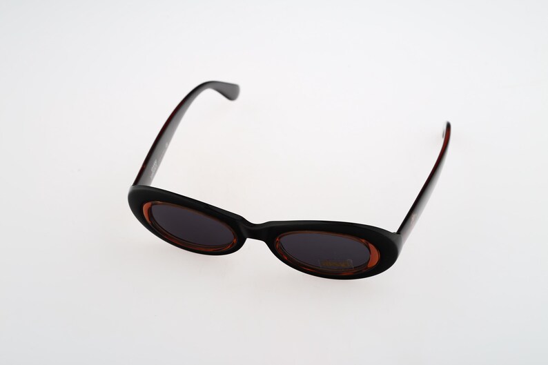 May include: Black oval sunglasses with brown tinted lenses. The sunglasses have a thin black frame.