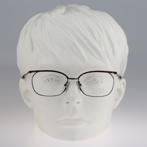 May include: A pair of tortoiseshell and silver eyeglasses with a square frame. The glasses are on a white mannequin head. The text "T.A.K.2" is printed on the right lens.