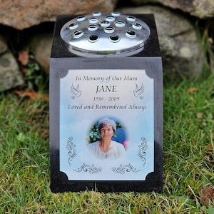 May include: Black granite memorial with a silver flower vase, a photo of a woman, and the inscription "In Memory of Our Mum JANE 1936 - 2009 Loved and Remembered Always".