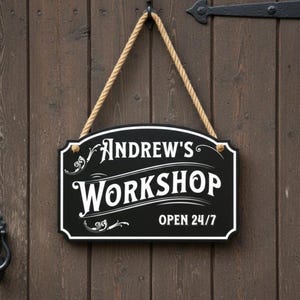 May include: A black and white sign reading "Andrew's Workshop OPEN 24/7" suspended by a rope. The sign is fixed to a dark brown wooden door. A black door knocker is visible on the left.