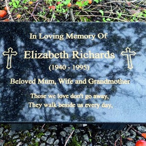 May include: Black granite memorial plaque with gold lettering. It reads "In Loving Memory Of Elizabeth Richards (1940-1995) Beloved Mum, Wife and Grandmother Those we love don't go away, They walk beside us every day."