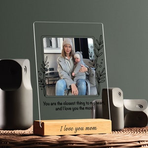 May include: A clear acrylic photo frame with a wooden base. The frame holds a photo of a woman and a child. The text "You are the closest thing to my heart, and I love you the most!" and "I love you mom" is printed on the frame.