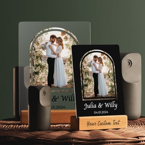 May include: Two black and white photo frames with a couple in a wedding setting. The frames are on a wooden stand with the text "Julia & Willy 04.01.2024 Your Custom Text" on the bottom.