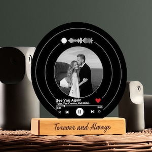 May include: A black and white photo of a couple is displayed on a round, black music record-shaped plaque with a white play button and a red heart. The plaque is on a wooden base with the words "Forever and Always" engraved on it.