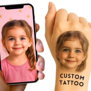 May include: A smartphone displaying a portrait of a young child with light brown hair wearing a pink shirt against a star-patterned background, alongside a temporary tattoo of the same child's face with the black text CUSTOM TATTOO below it.
