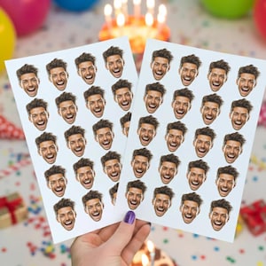 May include: Two sheets of stickers featuring a repeating pattern of a smiling face. The face has dark hair and a happy expression. The stickers are held in a hand with a purple painted fingernail. The background includes birthday decorations.