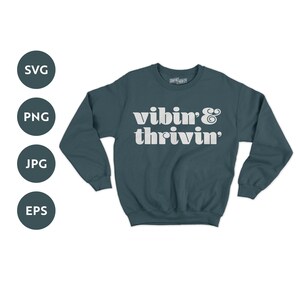 May include: A dark teal sweatshirt with the text "vibin' & thrivin'" in white. The text is in a retro font style.
