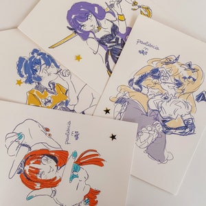 Peut inclure: Quatre cartes illustrées différentes avec un fond blanc. Chaque carte présente un personnage différent avec un style unique. Les personnages sont dessinés à l'encre noire avec des accents colorés. Le texte sur les cartes indique "Paulinicia" et "Mai 2022".