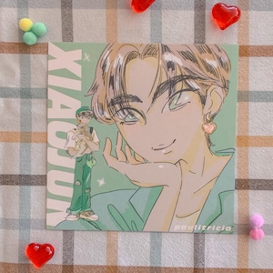 May include: A green and white illustrated card featuring a cartoon character with brown hair and green eyes. The character is wearing a green shirt and has a pink heart earring. The text "Xiaoou" is written in white on the left side of the card.