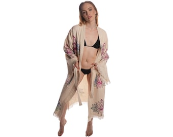 May include: A cream-colored robe with floral embroidery and a fringed hem. The robe is worn over a black bikini top.
