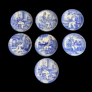 May include: Set of seven blue and white decorative plates. Each plate features a different illustration of a man in a period setting, with text labels such as "Soldier" and "Farmer". The plates have a circular shape and a detailed, hand-painted appearance.