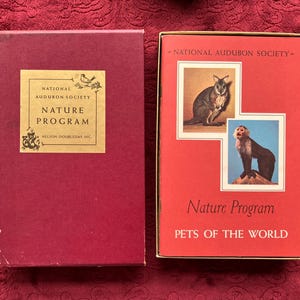 May include: Two vintage boxes from the National Audubon Society Nature Program. One box is burgundy with a gold label. The other box is red with images of a wallaby and monkey, and the text "Pets of the World."