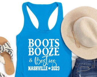 May include: Turquoise tank top with the text "Boots Booze & Besties Nashville 2023" in white. The tank top is laying on a white surface with a straw hat, denim shorts, and sandals.