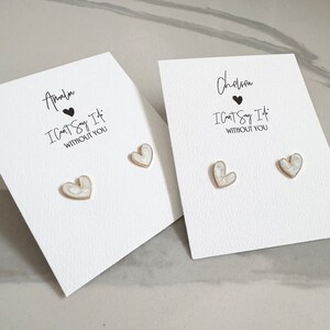 May include: Two pairs of white heart-shaped earrings with gold accents on a white card. The card has the text "I Can't Say It Without You" and the names "Chelsea" and "Amelia" written on them.