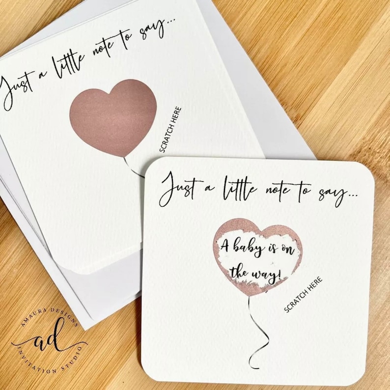 Puede incluir: Dos tarjetas blancas con un dise&ntilde;o de globo de coraz&oacute;n rosa. El texto en las tarjetas dice "Just a little note to say..." y "A baby is on the way!" con las palabras "Scratch Here" debajo de los globos.