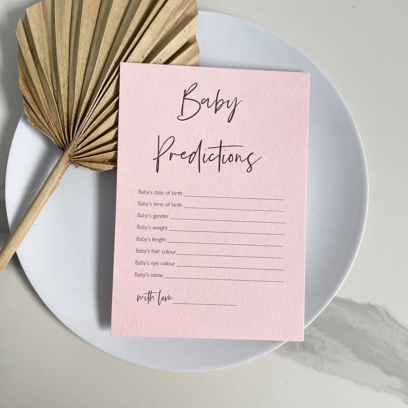 May include: A pink card with the text "Baby Predictions" in black cursive writing. The card has a list of predictions for a baby, including date of birth, time of birth, gender, weight, length, hair colour, eye colour, and name. The card ends with the text "with love" in black cursive writing.