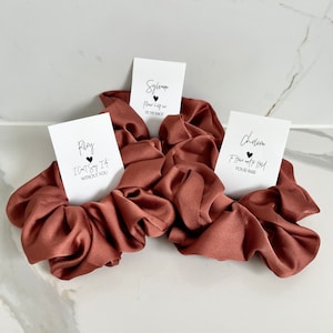 May include: Three brown satin scrunchies with white cards attached. The cards have black text that reads "Ray I can't say I'd without you", "Sylvan Please help me tie the knot", and "Charen I have got this your hair".