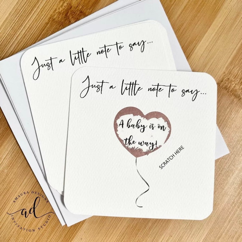 Puede incluir: Una tarjeta blanca con el texto "Just a little note to say..." y un globo rosa en forma de coraz&oacute;n con el texto "A baby is on the way!" y las palabras "Scratch Here" debajo del globo.