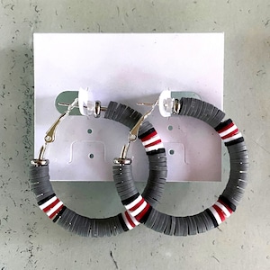 May include: A pair of gray hoop earrings with red and white stripes. The earrings are made of stacked round beads.