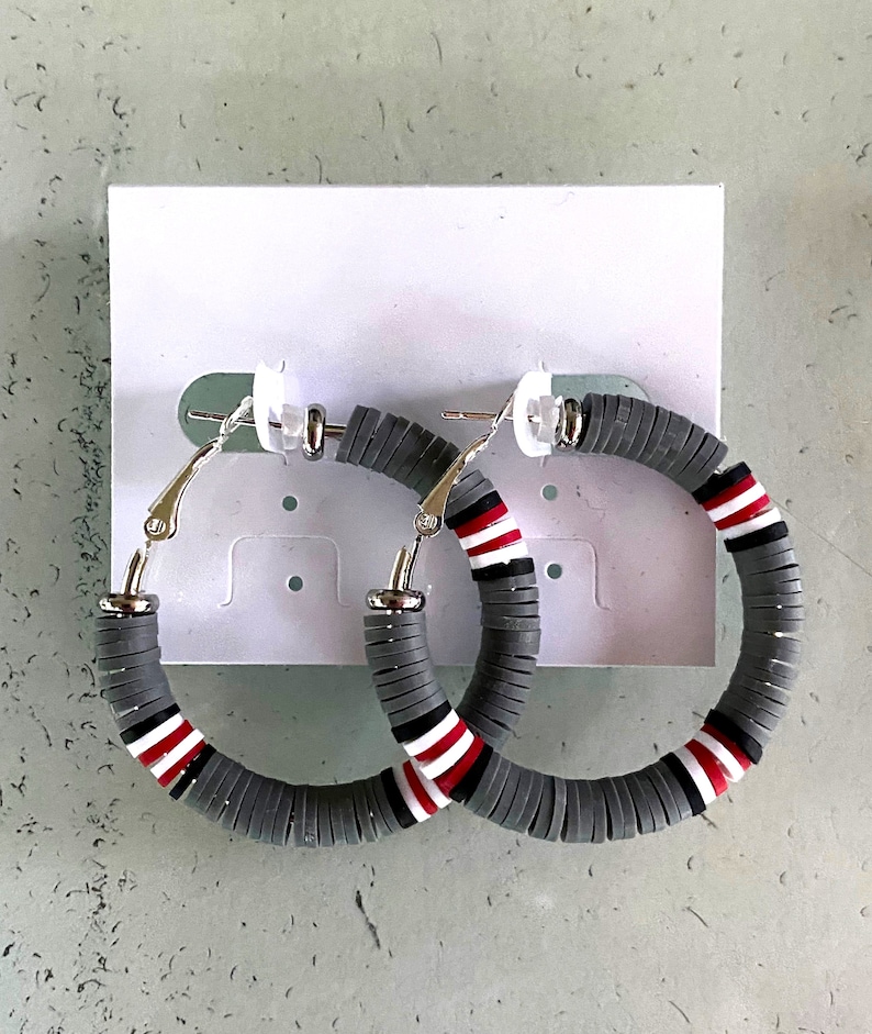 May include: A pair of gray hoop earrings with red and white stripes. The earrings are made of stacked round beads.