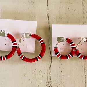 May include: Two pairs of red and white hoop earrings with silver clasps. The larger pair is on the left and the smaller pair is on the right.