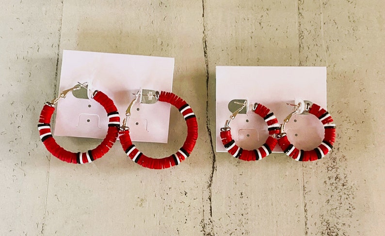 May include: Two pairs of red and white hoop earrings with silver clasps. The larger pair is on the left and the smaller pair is on the right.