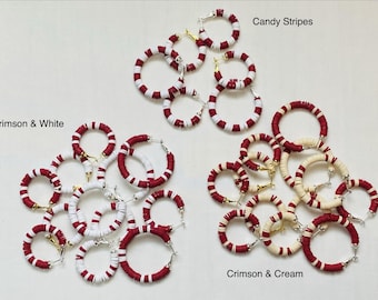 May include: An assortment of hoop earrings in red and white, red and cream, and red and white striped designs. The earrings are arranged in clusters, with the text "Candy Stripes", "Crimson & White", and "Crimson & Cream" visible.