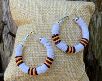 May include: A pair of hoop earrings made of white and orange polymer clay. The earrings are stacked with small, round beads and have a silver hook closure.