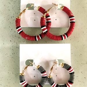 May include: Two pairs of hoop earrings with red and white stripes and gray and white stripes. The earrings are made of polymer clay and have gold-toned hoops.