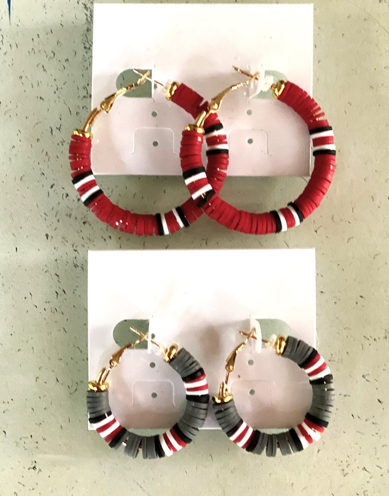 May include: Two pairs of hoop earrings with red and white stripes and gray and white stripes. The earrings are made of polymer clay and have gold-toned hoops.