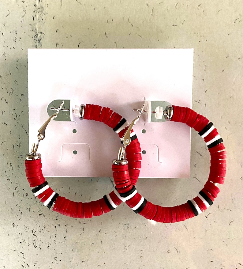 May include: A pair of red and white hoop earrings with a silver clasp. The earrings are made of stacked round beads.