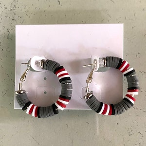 May include: A pair of hoop earrings with a gray, white, and red striped design. The earrings are made of a lightweight material and have a silver-toned finish.