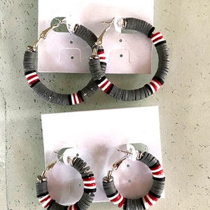 May include: Two pairs of hoop earrings with a gray, white, and red color scheme. The earrings are made of a layered material that resembles beads.