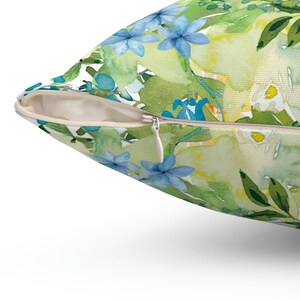 Op de afbeelding: Een kussen met een rits heeft een aquarel bloemenpatroon met blauwe, groene en gele bloemen.