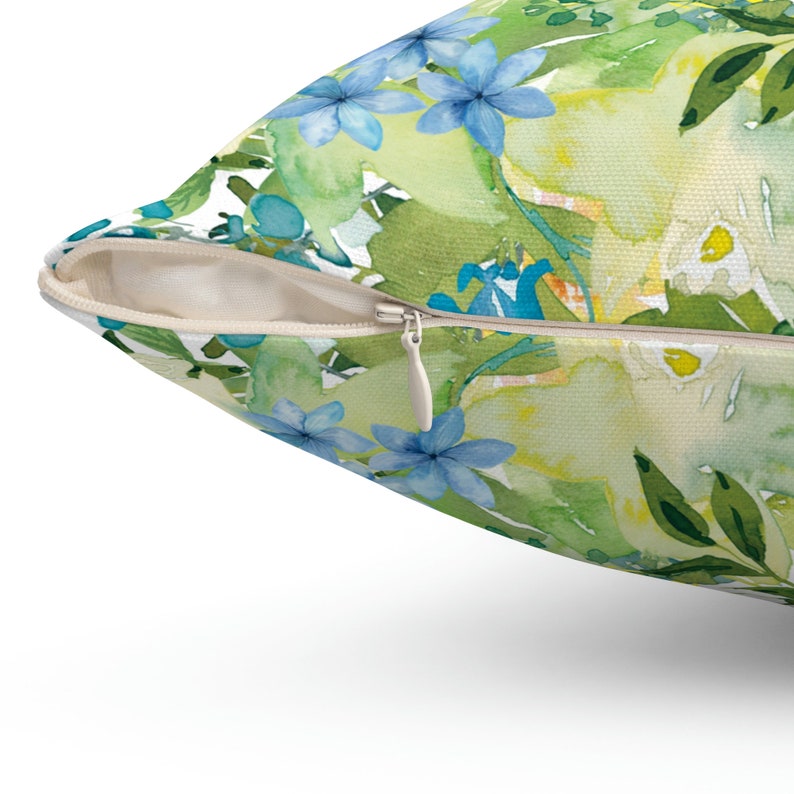 Op de afbeelding: Een kussen met een rits heeft een aquarel bloemenpatroon met blauwe, groene en gele bloemen.