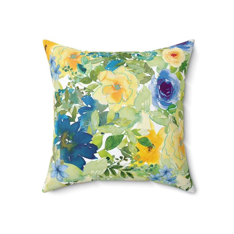 Op de afbeelding: Een vierkant kussen met een bloemenpatroon met gele, blauwe en groene aquarelbloemen op een witte achtergrond.