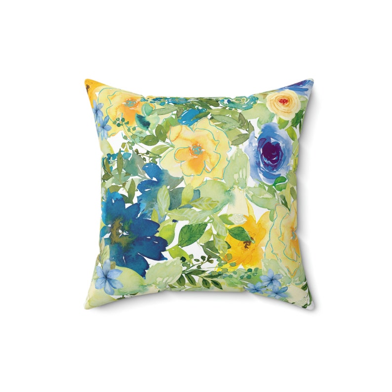Op de afbeelding: Een vierkant kussen met een bloemenpatroon met gele, blauwe en groene aquarelbloemen op een witte achtergrond.