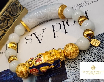 May include: A white jade bracelet with gold accents and a gold charm featuring a mythical creature. The charm has blue and red enamel details and Chinese characters. The bracelet is on a white and black patterned surface.
