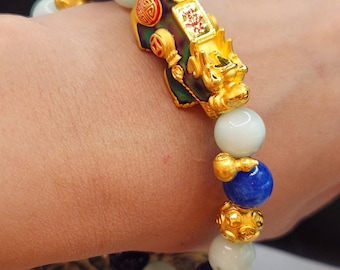 May include: A gold bracelet with a jade and blue stone design. The bracelet features a gold charm in the shape of a mythical creature with red and gold accents. The charm has Chinese characters on it.