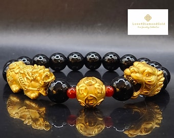 Könnte beinhalten: Ein goldenes Armband mit schwarzen Perlen und zwei goldenen Löwenanhängern. Das Armband hat außerdem einen goldenen Anhänger mit chinesischen Schriftzeichen. Das Armband liegt auf einer schwarzen Oberfläche. Love4DiamondGold Fine Jewelry Collection.