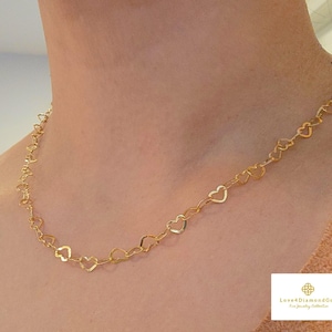 Pode incluir: Um delicado colar de ouro com uma série de elos em forma de coração. O colar é exibido no pescoço de uma pessoa, mostrando seu design. Joias da coleção Love4DiamondGold Fine Jewelry.