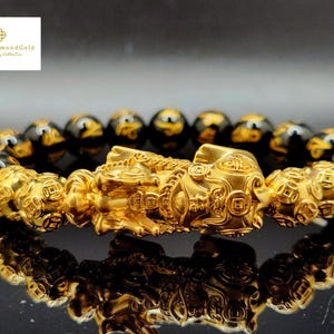 May include: A gold-coloured bracelet with detailed Pixiu charms and black and gold beads. The bracelet features a central Pixiu design against a dark background. The Love4DiamondGold logo is in the upper left corner.