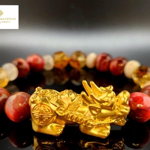 May include: A gold-coloured Pixiu charm bracelet featuring a variety of gemstone beads in shades of red, yellow, and white. The Pixiu is a mythical creature, and the bracelet is likely fine jewellery.