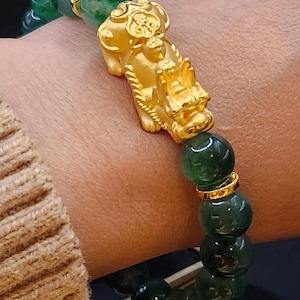 Könnte beinhalten: Ein Armband mit Jadeperlen und einem goldenen Pixiu-Anhänger. Das Armband hat dunkelgrüne Jadeperlen und goldene Akzente. Der Pixiu-Anhänger ist aufwendig detailliert. Es ist ein Schmuckstück.
