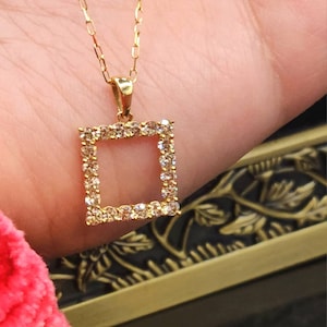 May include: A gold chain necklace with a square pendant set with small clear stones.