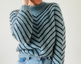 Puede incluir: Un suéter azul y negro a rayas con un patrón de chevron. El suéter tiene un cuello alto y mangas largas.