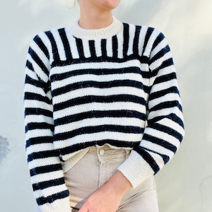 Puede incluir: Un suéter de rayas blancas y negras con cuello redondo. El suéter está hecho de un material suave y peludo.