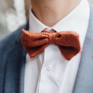 Könnte beinhalten: Nahaufnahme eines gehäkelten Fliege in verbranntem Orange, getragen mit einem weißen Hemd und einem blauen Blazer.